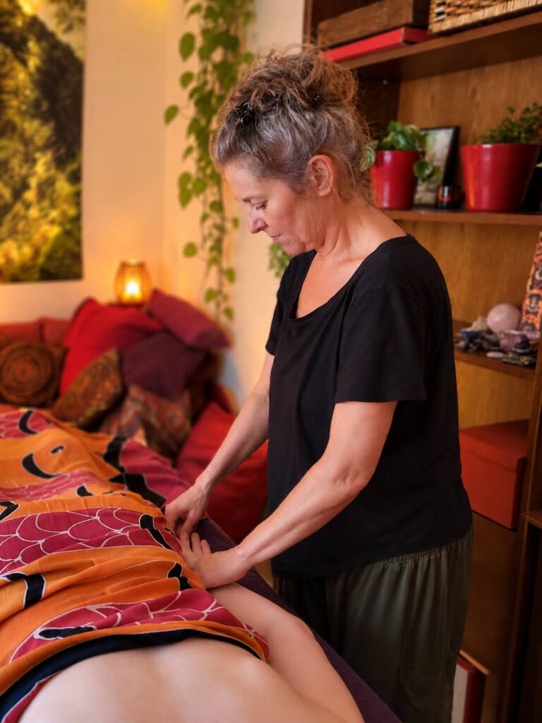 Monique staat aan de behandeltafel en legt haar handen op de rug van een cliënte